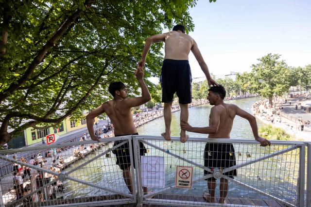 A man prepares to jump from a bridge into the Canal Saint-Martin, next to a sign prohibiting diving, as France experiences a heatwave, in Paris on July 12, 2026. (Photo by Behrouz MEHRI / AFP)