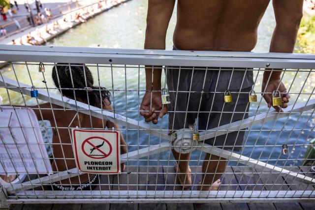 A man stands next to a sign prohibiting diving as they wait to jump from a bridge into the Canal Saint-Martin as France experiences a heatwave, in Paris on July 12, 2026. (Photo by Behrouz MEHRI / AFP)