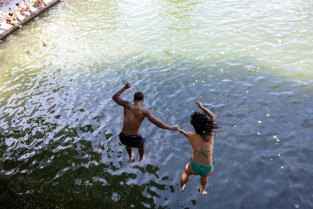 A couple jumps from a bridge into the Canal Saint-Martin as France experiences a heatwave, in Paris on July 12, 2026. (Photo by Behrouz MEHRI / AFP)