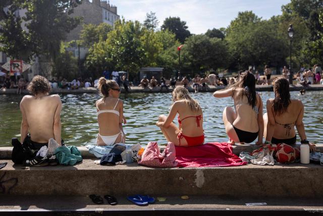 People sit by the Canal Saint-Martin as France experiences a heatwave, in Paris on July 12, 2026. (Photo by Behrouz MEHRI / AFP)