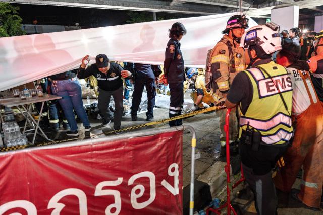 Emergency workers stand next to a white fabric displayed at the scene after a massive fire engulfed a bar in Bangkok, early on July 13, 2026. A fire in a bar in the Thai capital Bangkok killed at least 27 people late Sunday night, Prime Minister Anutin Charnvirakul told local media. (Photo by chanakarn LAOSARAKHAM / AFP)