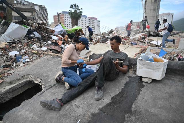 A nurse provides medical assistance to a volunteer rescuer during a search operation at the collapsed Obras del Poder Popular (OPP) building in Caraballeda, La Guaira state, Venezuela, on July 12, 2026, following twin earthquakes that struck the region. The twin earthquakes that struck Venezuela on June 24 had left nearly 4,500 people dead as of July 12, while much of the affected population continued to live in camps, according to official figures. (Photo by Juan BARRETO / AFP)