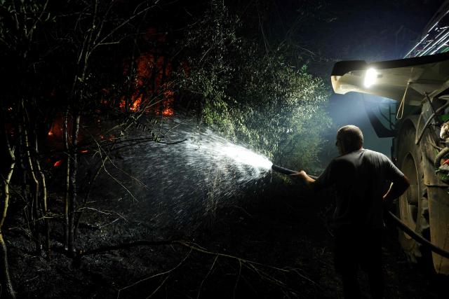 A farmer sprays water in the forest of Fontainebleau, southeast of Paris, after a forest fire broke out late afternoon in Noisy-sur-Ecole on July 12, 2026. The fire that has been raging in the Fontainebleau forest, in the south of the Paris region, is of "exceptional magnitude" said the sub-prefect for the area. Whilst two water-bombing aircraft have been deployed to tackle the blaze, a first for Paris' Ile-de-France region, some 400 firefighters are on the ground battling the fire, which, shortly before 11.00 pm, had spread across more than 300 hectares and was still "spreading", the official added during a press briefing. (Photo by GEOFFROY VAN DER HASSELT / AFP)