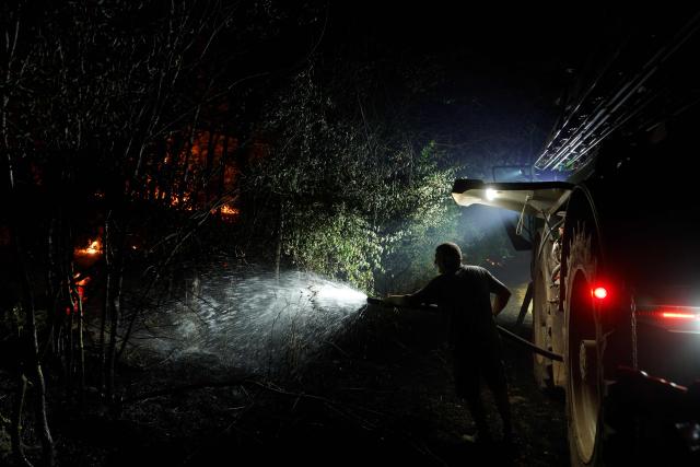 A farmer sprays water in the forest of Fontainebleau, southeast of Paris, after a forest fire broke out late afternoon in Noisy-sur-Ecole on July 12, 2026. The fire that has been raging in the Fontainebleau forest, in the south of the Paris region, is of "exceptional magnitude" said the sub-prefect for the area. Whilst two water-bombing aircraft have been deployed to tackle the blaze, a first for Paris' Ile-de-France region, some 400 firefighters are on the ground battling the fire, which, shortly before 11.00 pm, had spread across more than 300 hectares and was still "spreading", the official added during a press briefing. (Photo by GEOFFROY VAN DER HASSELT / AFP)