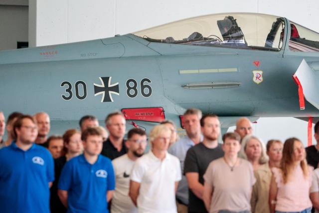 Civil workers stand in front of a Eurofighter Typhoon EF2000 30-86 jet of the German air force during the visit of the German Defence Minister at the Wittmund air base, home of the Tactical Air Force Wing (Taktisches Luftwaffengeschwader) 71 'Richthofen', in Wittmund, northern Germany, on July 13, 2026. Wittmund air base is also home of the Quick Reaction Alert (QRA) of the German air force for northern Germany. (Photo by FOCKE STRANGMANN / AFP)