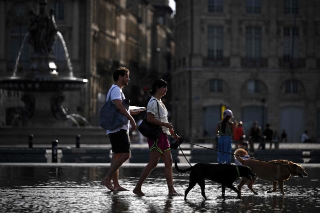 Pedestrians walk their dogs through the Miroir d'eau reflecting pool amid a heatwave, in Bordeaux, southwestern France on July 12, 2026. Twenty-six million French people remain under a red heatwave alert ahead of a let-up on Tuesday, though this will not mark the end of the third heatwave to hit France in less than two months. (Photo by Christophe ARCHAMBAULT / AFP)