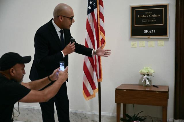 A reporter works as flowers are left outside the office of the late US Senator Lindsey Graham, Republican from South Carolina, on Capitol Hill in Washington, DC, on July 13, 2026. Graham, a South Carolina Republican and key Trump ally who was elected to the Senate four times, died aged 71 following a "brief and sudden illness," his office said on July 12, 2026. Graham made a name for himself with his work on foreign policy and in recent years urged both the Trump and Biden administrations to back Kyiv's fight against Russia's invasion. He was a staunch supporter of the Iran war. (Photo by Brendan SMIALOWSKI / AFP)