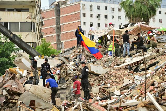 Rescue workers and relatives of missing people look for bodies amid the rubble of a collapsed building in Caraballeda, La Guaira State, Venezuela on July 13, 2026, following the June 24 twin earthquakes. The official death toll from Venezuela's devastating twin earthquakes rose to nearly 4,500 on July 12, 2026, as the government reported more than 19,500 people were now living in camps due to the destruction. (Photo by MARTIN BERNETTI / AFP)