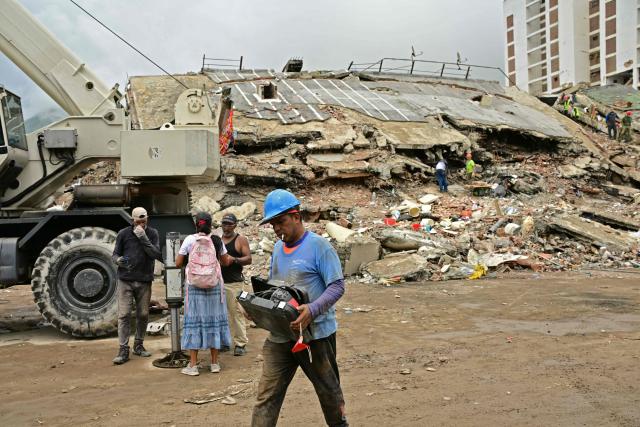 Relatives of missing people remain near a backhoe used at a collapsed building in Caraballeda, La Guaira State, Venezuela on July 13, 2026, following the June 24 twin earthquakes. The official death toll from Venezuela's devastating twin earthquakes rose to nearly 4,500 on July 12, 2026, as the government reported more than 19,500 people were now living in camps due to the destruction. (Photo by MARTIN BERNETTI / AFP)