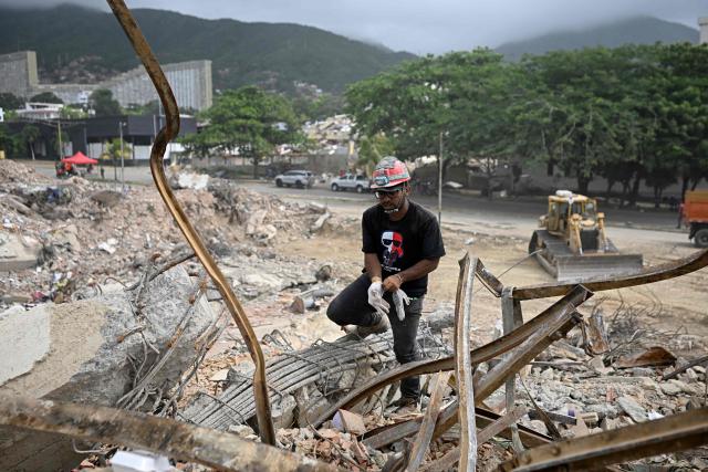 Daniel Gonzalez searches for his cousin Felix Astudillo amid the rubble of a collapsed building in Los Corales, La Guaira state, Venezuela, on July 13, 2026, following twin earthquakes that struck the region. The death toll from the twin earthquakes that struck Venezuela nearly three weeks ago has surpassed 4,500, while the number of injured remains at about 17,000, according to the latest government report released on July 13. (Photo by Federico PARRA / AFP)