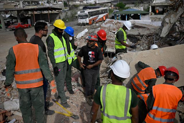 Daniel Gonzalez (C) talks with Venezuelan military personnel after finding the body of his cousin Felix Astudillo amid the rubble of a collapsed building in Los Corales, La Guaira state, Venezuela, on July 13, 2026, following twin earthquakes that struck the region. The death toll from the twin earthquakes that struck Venezuela nearly three weeks ago has surpassed 4,500, while the number of injured remains at about 17,000, according to the latest government report released on July 13. (Photo by Federico PARRA / AFP)