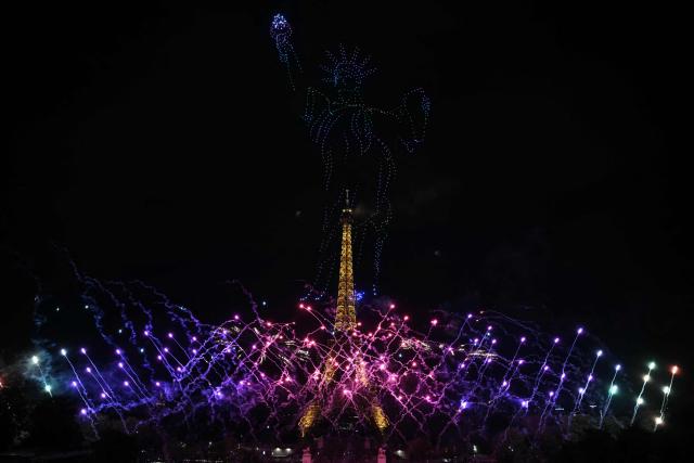 Fireworks explode as drones form a depiction of the Statue of Liberty around the Eiffel Tower during a choreographed show marking Bastille Day in Paris on July 13, 2026, on the eve of the annual Bastille Day parade in the French capital. (Photo by Lou BENOIST / AFP)