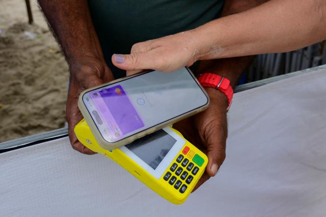 A woman pays for a purchase at Copacabana Beach using Brazil's Pix instant payment system in Rio de Janeiro, Brazil, on July 9, 2026. It started as a payment tool and became a source of national pride. In just a few years, Brazil's PIX established itself as the dominant payment method in Latin America's largest economy. But in the process, it stepped on the toes of powerful interests in the United States. (Photo by Pablo PORCIUNCULA / AFP)