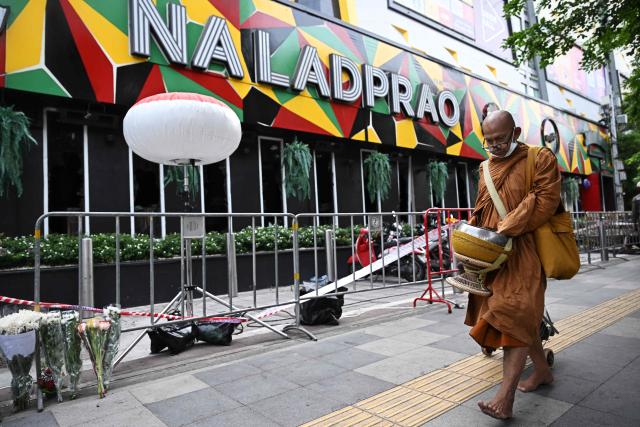 A Buddhist monk walks past the Rong Beer Na Lat Phrao bar in Bangkok on July 14, 2026. Investigators combed on July 13 through the wreckage of a huge fire at a Bangkok bar that killed at least 28 people, as relatives began the grim task of identifying the dead. (Photo by Lillian SUWANRUMPHA / AFP)