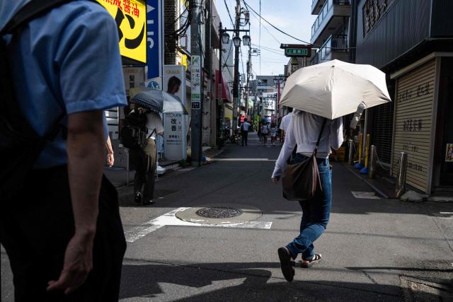 Commuters use umbrellas to take shelter from the sun as they walk to the metro station on a hot morning in Tokyo on July 14, 2026. (Photo by Andrew CABALLERO-REYNOLDS / AFP)