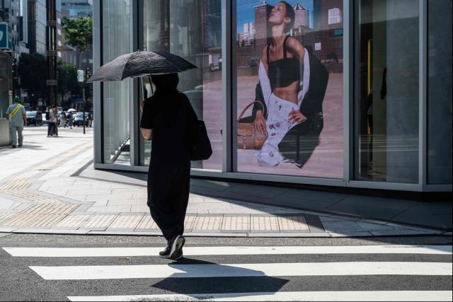 A woman uses an umbrella to take shelter from the sun as she walks past a Prada advertisement on a hot morning in Tokyo on July 14, 2026. (Photo by Andrew CABALLERO-REYNOLDS / AFP)