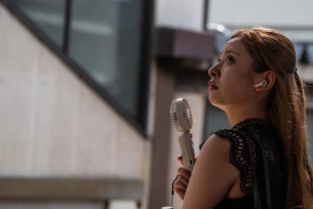 A woman uses a portable fan to keep cool as she waits for a train on a hot morning in Tokyo on July 14, 2026. (Photo by Andrew CABALLERO-REYNOLDS / AFP)