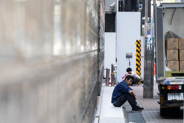 A delivery driver takes a smoking break in the shade on a hot morning in Tokyo on July 14, 2026. (Photo by Andrew CABALLERO-REYNOLDS / AFP)