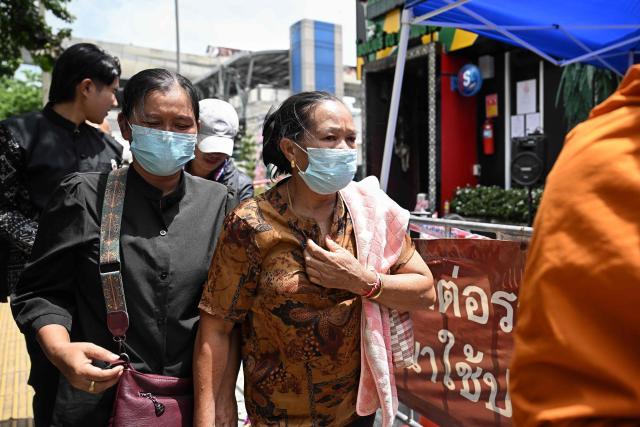 Relatives of victim Sittipong Chaiyo, 28, walk in front of the Rong Beer Na Lat Phrao bar in Bangkok on July 14, 2026. Stricken relatives of the victims of a huge Bangkok bar fire claimed their bodies July 14 as the death toll rose to 30, even as others held out hope that their loved ones were still alive. (Photo by Lillian SUWANRUMPHA / AFP)
