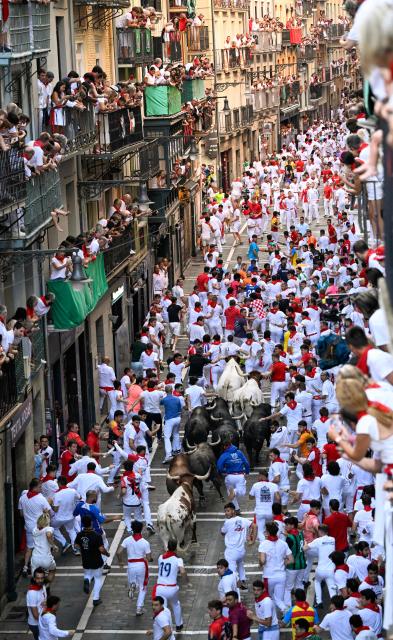Participants run ahead of bulls from the Jandilla bull ranch during the eighth running of the bulls of the San Fermin festival in Pamplona, northern Spain, on July 14, 2026. Thousands of people every year attend the week-long festival and its famous 'encierros', or running of the bulls, in which six bulls are released at 8:00 a.m. evey day to run from their corral to the bullring through the narrow streets of the old town over an 850 meters (yards) course while runners ahead of them try to stay close to the bulls without falling over or being gored. (Photo by ANDER GILLENEA / AFP)