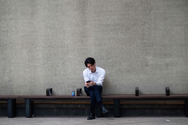 A man sits in the shade and checks his phone on a hot day in Tokyo on July 14, 2026. (Photo by Andrew CABALLERO-REYNOLDS / AFP)