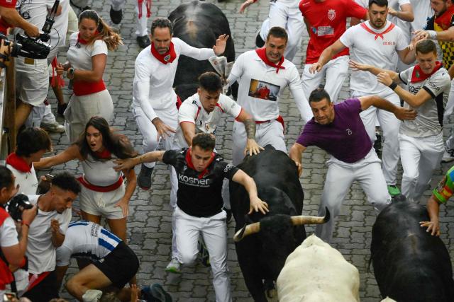 Participants run ahead of bulls from the Jandilla bull ranch during the eighth running of the bulls of the San Fermin festival in Pamplona, northern Spain, on July 14, 2026. Thousands of people every year attend the week-long festival and its famous 'encierros', or running of the bulls, in which six bulls are released at 8:00 a.m. evey day to run from their corral to the bullring through the narrow streets of the old town over an 850 meters (yards) course while runners ahead of them try to stay close to the bulls without falling over or being gored. (Photo by Miguel RIOPA / AFP)