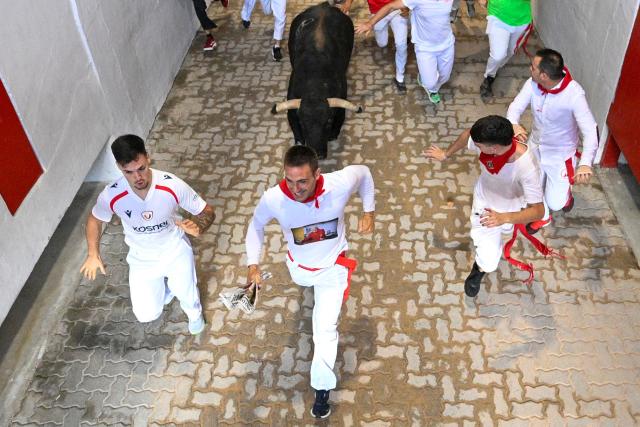 Participants run ahead of bulls from the Jandilla bull ranch during the eighth running of the bulls of the San Fermin festival in Pamplona, northern Spain, on July 14, 2026. Thousands of people every year attend the week-long festival and its famous 'encierros', or running of the bulls, in which six bulls are released at 8:00 a.m. evey day to run from their corral to the bullring through the narrow streets of the old town over an 850 meters (yards) course while runners ahead of them try to stay close to the bulls without falling over or being gored. (Photo by Miguel RIOPA / AFP)