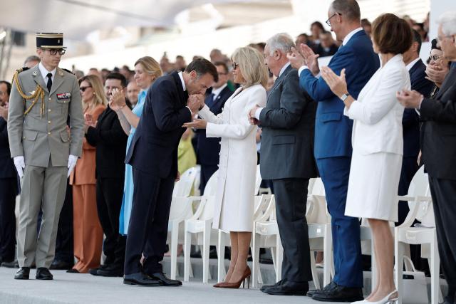 France's President Emmanuel Macron (C-L) kisses the hand of his wife Brigitte Macron (C-R) next to Ukraine's President Volodymyr Zelensky (3L) and his wife Olena Zelenska (2L), President of the French National Assembly Yael Braun-Pivet (4L), President of the French Senate Gerard Larcher (4R) and German Chancellor Friedrich Merz (3R) on the Place de la Concorde during the annual Bastille Day military parade in Paris on July 14, 2026. (Photo by Benoit Tessier / POOL / AFP)
