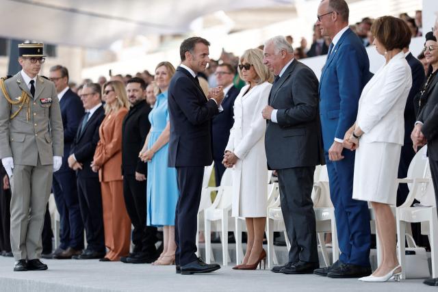 France's President Emmanuel Macron (C) gestures next to British Prime Minister Keir Starmer (L), Ukraine's President Volodymyr Zelensky (3L) and his wife Olena Zelenska (2L), President of the French National Assembly Yael Braun-Pivet (4L), French President's wife Brigitte Macron (C-R), President of the French Senate Gerard Larcher (3R) and German Chancellor Friedrich Merz (2R) on the Place de la Concorde during the annual Bastille Day military parade in Paris on July 14, 2026. (Photo by Benoit Tessier / POOL / AFP)