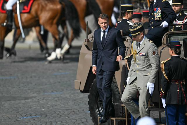 France's President Emmanuel Macron (L) steps dowm from the command car during the annual Bastille Day military parade on the Champs-Elysees Avenue in Paris on July 14, 2026. (Photo by LOU BENOIST / AFP)