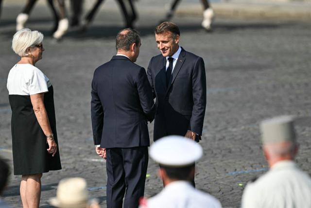 France's President Emmanuel Macron (R) shakes hands with France's Prime Minister Sebastien Lecornu (C) next to France's Defence Minister Catherine Vautrin during the annual Bastille Day military parade on the Champs-Elysees Avenue in Paris on July 14, 2026. (Photo by LOU BENOIST / AFP)