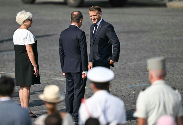 France's President Emmanuel Macron (R) speaks with France's Prime Minister Sebastien Lecornu (C) and France's Defence Minister Catherine Vautrin during the annual Bastille Day military parade on the Champs-Elysees Avenue in Paris on July 14, 2026. (Photo by LOU BENOIST / AFP)