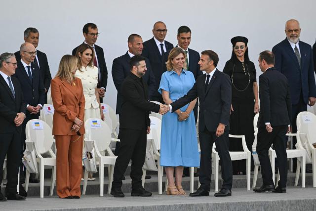 France's President Emmanuel Macron (C-R) shakes hands with Ukraine's President Volodymyr Zelensky (C-L) next to President of the French National Assembly Yael Braun-Pivet (C) on the Place de la Concorde during the annual Bastille Day military parade in Paris on July 14, 2026. (Photo by LOU BENOIST / AFP)