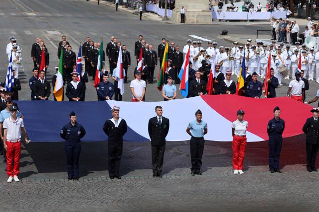 Troops of the Coalition of volunteers of invited foreign nations display a French flag as they take part in the annual Bastille Day military parade on the Champs-Elysees Avenue in Paris on July 14, 2026. (Photo by Ludovic MARIN / AFP)