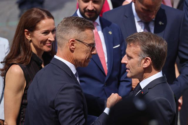 France's President Emmanuel Macron (R) greets Finland's President Alexander Stubb (C) and his wife Suzanne Innes-Stubb during the annual Bastille Day military parade on the Champs-Elysees Avenue in Paris on July 14, 2026. (Photo by Ludovic MARIN / AFP)