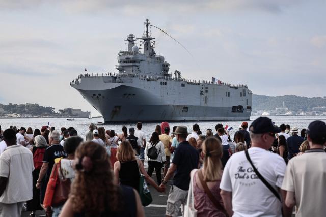 Relatives and spectators wait for the arrival of the amphibious helicopter carrier (PHA) 'Dixmude' in the port of Toulon, south-eastern France on July 14, 2026, as the "Jeanne d’Arc" task force concludes a five-month mission. Nearly 800 service members took part in this deployment, including 162 officer cadets. This annual deployment marks the culmination of the training of French and foreign officer cadets at the Naval Academy. (Photo by Thibaud MORITZ / AFP)