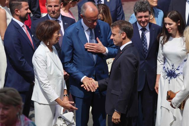 France's President Emmanuel Macron (R) greets German Chancellor Friedrich Merz (C) and his wife Charlotte Merz (L) during the annual Bastille Day military parade on the Champs-Elysees Avenue in Paris on July 14, 2026. (Photo by Ludovic MARIN / AFP)