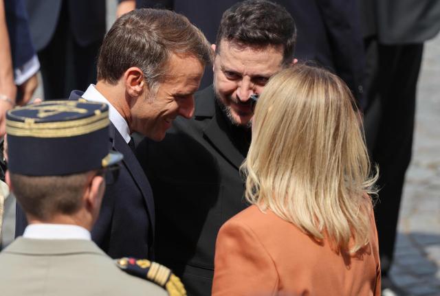 France's President Emmanuel Macron (L) speaks with Ukraine's President Volodymyr Zelensky (C) and his wife Ukraine's Olena Zelenska during the annual Bastille Day military parade on the Champs-Elysees Avenue in Paris on July 14, 2026. (Photo by Ludovic MARIN / AFP)