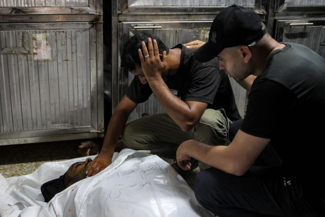 EDITORS NOTE: Graphic content / Men grieve by the body of one of several victims who were killed after a police station was was hit by Israeli bombardment in the Jabalia camp for Palestinian refugees in the northern Gaza Strip, ahead of the funeral at a morgue at al-Shifa Hosital in Gaza City on July 14, 2026. Gaza's civil defence agency and the hospital said that the Israeli airstrike on the police station in northern Gaza killed eight people on July 14, including a woman officer. In a statement condemning the strike, Palestinian Islamist movement Hamas, which controls Gaza's police force, said that the police station chief was among those killed. (Photo by Omar AL-QATTAA / AFP)