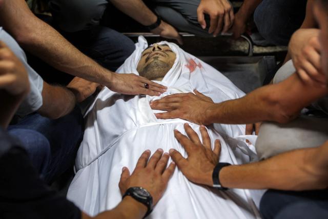 EDITORS NOTE: Graphic content / Mourners bid farewell to the body of one of several victims who were killed after a police station was was hit by Israeli bombardment in the Jabalia camp for Palestinian refugees in the northern Gaza Strip, as they gather ahead of the funeral at a morgue at al-Shifa Hosital in Gaza City on July 14, 2026. Gaza's civil defence agency and the hospital said that the Israeli airstrike on the police station in northern Gaza killed eight people on July 14, including a woman officer. In a statement condemning the strike, Palestinian Islamist movement Hamas, which controls Gaza's police force, said that the police station chief was among those killed. (Photo by Omar AL-QATTAA / AFP)