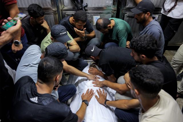EDITORS NOTE: Graphic content / Mourners bid farewell to the body of one of several victims who were killed after a police station was was hit by Israeli bombardment in the Jabalia camp for Palestinian refugees in the northern Gaza Strip, as they gather ahead of the funeral at a morgue at al-Shifa Hosital in Gaza City on July 14, 2026. Gaza's civil defence agency and the hospital said that the Israeli airstrike on the police station in northern Gaza killed eight people on July 14, including a woman officer. In a statement condemning the strike, Palestinian Islamist movement Hamas, which controls Gaza's police force, said that the police station chief was among those killed. (Photo by Omar AL-QATTAA / AFP)