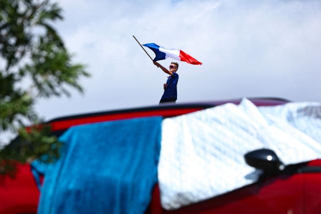 A spectator waves a French flag along the race route during the 10th stage of the 113th edition of the Tour de France cycling race, 166,6 km between Aurillac and Le Lioran in the Massif Central, on July 14, 2026. (Photo by Anne-Christine POUJOULAT / AFP)