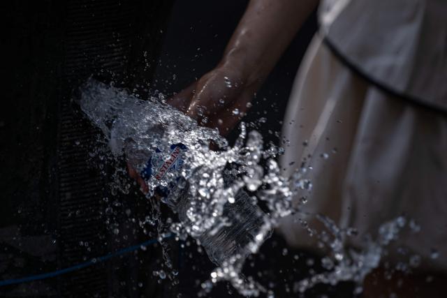 A tourist attempts to refill a plastic water bottle from a dysfunctioning public water fountain amid a heatwave in Paris on July 14, 2026. The Paris region, and large parts of the rest of France, is currently experiencing the third heatwave since May 2026, increasing the risk of fires. The three heatwaves have seen temperature records broken in several countries across Europe and have caused thousands of excess deaths, according to estimates in Belgium, Britain, France and Spain. (Photo by Martin LELIEVRE / AFP)