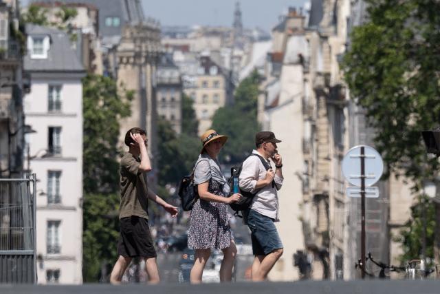 Pedestrians cross a street amid a heatwave in Paris on July 14, 2026. The Paris region, and large parts of the rest of France, is currently experiencing the third heatwave since May 2026, increasing the risk of fires. The three heatwaves have seen temperature records broken in several countries across Europe and have caused thousands of excess deaths, according to estimates in Belgium, Britain, France and Spain. (Photo by Martin LELIEVRE / AFP)