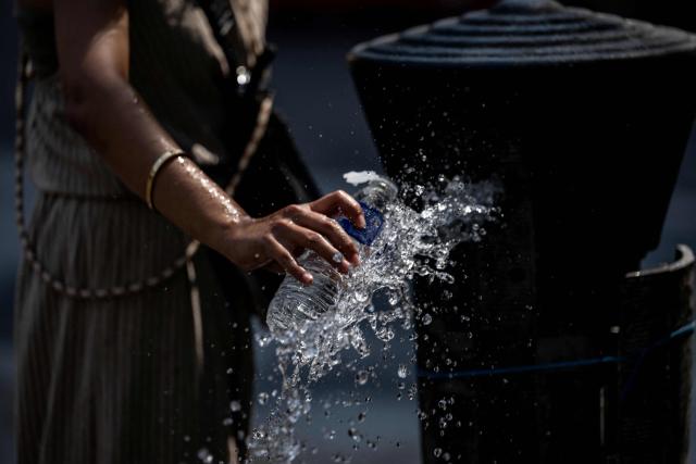 A tourist attempts to refill a plastic water bottle from a dysfunctioning public water fountain amid a heatwave in Paris on July 14, 2026. The Paris region, and large parts of the rest of France, is currently experiencing the third heatwave since May 2026, increasing the risk of fires. The three heatwaves have seen temperature records broken in several countries across Europe and have caused thousands of excess deaths, according to estimates in Belgium, Britain, France and Spain. (Photo by Martin LELIEVRE / AFP)