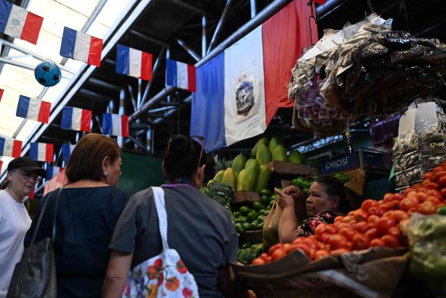 People visit the Duenas Market where vendors display flags in support of the French national football team during the FIFA World Cup semifinals between France and Spain, in Santa Tecla, El Salvador, on July 14, 2026. As the tournament reaches its final stages, many market vendors have openly embraced their favorite teams, decorating stalls and market aisles with flags, jerseys and colors in celebration of the competing nations. (Photo by Marvin RECINOS / AFP)