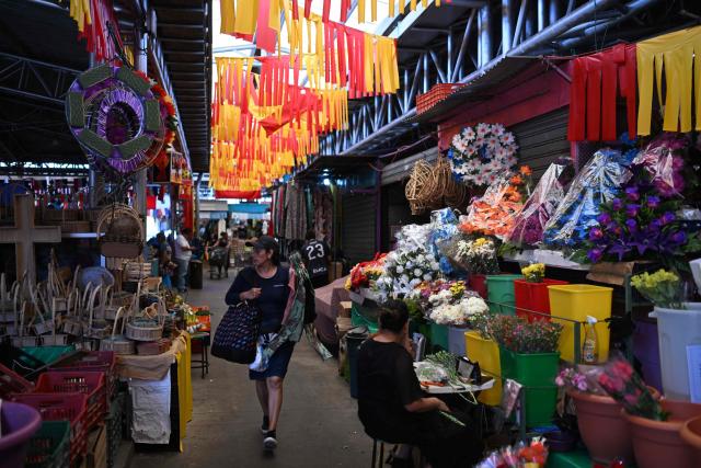 A woman walks past stalls selling flowers and goods at the Duenas Market decorated with Spanish national colors during the FIFA World Cup semifinals between France and Spain, in Santa Tecla, El Salvador, on July 14, 2026. As the tournament reaches its final stages, many market vendors have openly embraced their favorite teams, decorating stalls and market aisles with flags, jerseys and colors in celebration of the competing nations. (Photo by Marvin RECINOS / AFP)