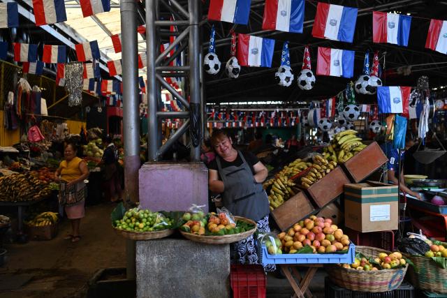 Vendors wait for customers at the Duenas Market where they displayed flags in support of the French national football team during the FIFA World Cup semifinals between France and Spain, in Santa Tecla, El Salvador, on July 14, 2026. As the tournament reaches its final stages, many market vendors have openly embraced their favorite teams, decorating stalls and market aisles with flags, jerseys and colors in celebration of the competing nations. (Photo by Marvin RECINOS / AFP)