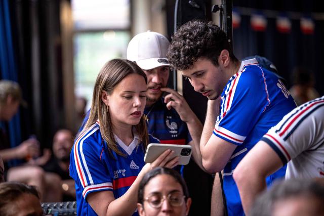 French fans watch the World Cup semi-final game between France and Spain on a phone during minor technical difficulties during an event organized by the French consulate at Robin des Bois in Lafontaine Park in Montreal, Quebec, Canada, on July 14, 2026. (Photo by ANDREJ IVANOV / AFP)