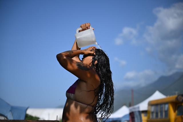 A woman displaced following twin earthquakes that struck the region bathes with water from a tank at 'Ciudad Carpita', an improvised shelter in Mare Abajo, La Guaira state, Venezuela, on July 14, 2026, . The death toll from the deadly earthquakes that hit Venezuela on June 14 has surpassed 4,700, while almost 17,000 people have been injured, an official report released on July 14 stated. (Photo by Raul ARBOLEDA / AFP)